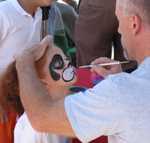 a child having her face painted with a mouse design